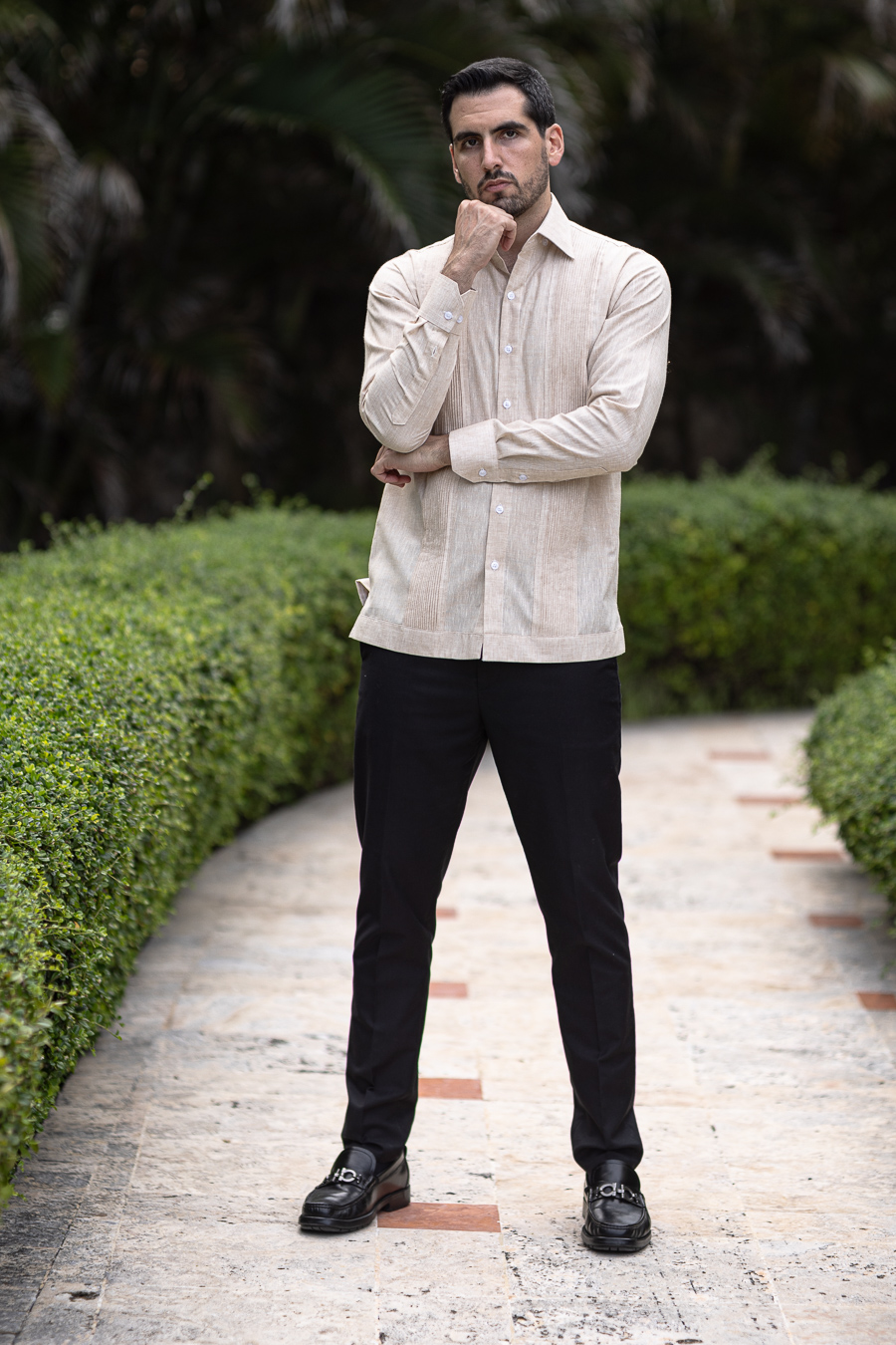 Model wearing a sand linen guayabera, full length, in a garden atelier setting